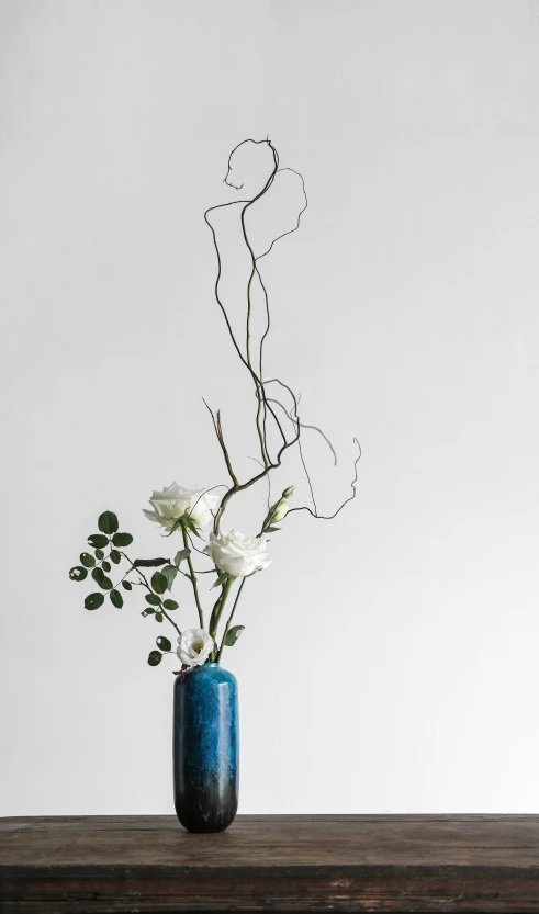 a white flower bouquet with vines in blue vase