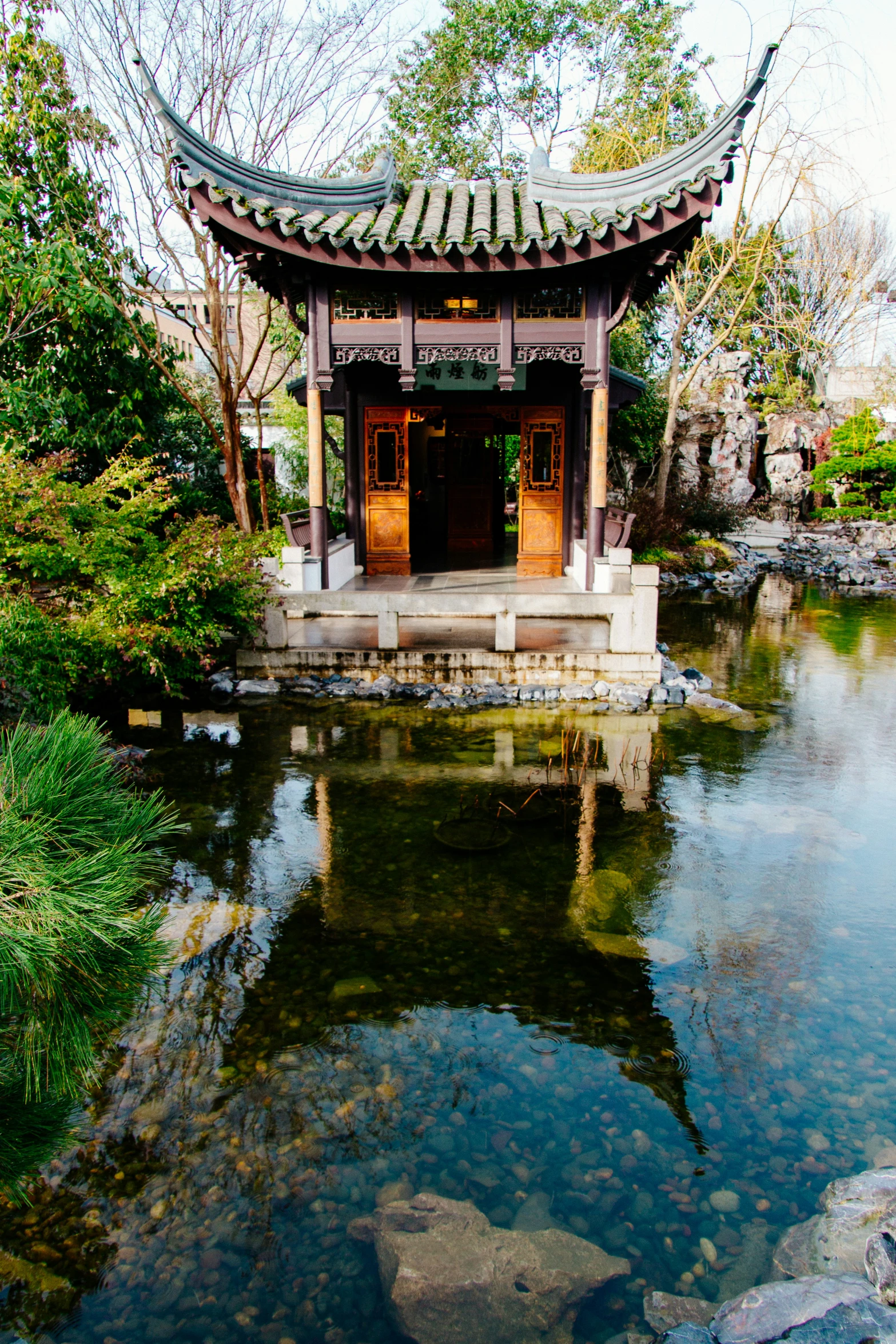 an oriental pagoda sits above a pond in the middle of a garden