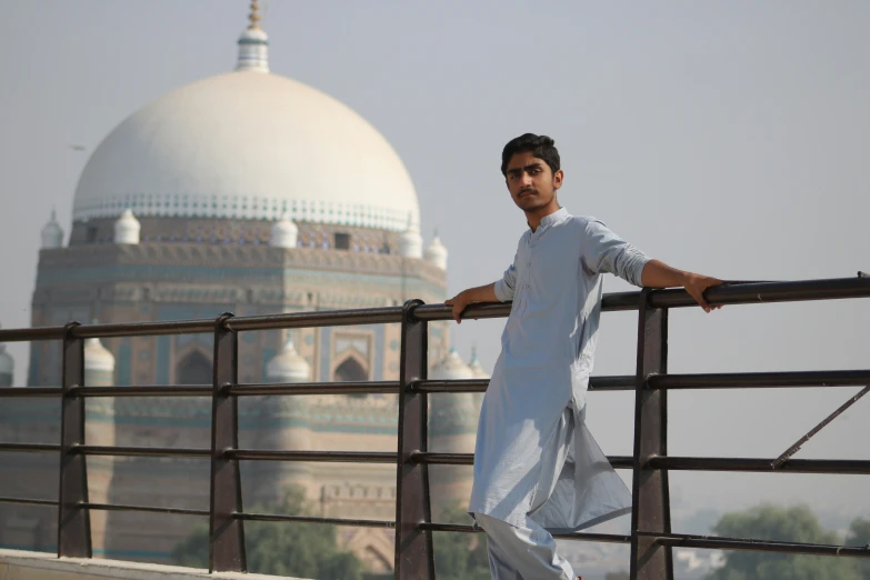 a man standing next to a railing with a tall building in the background