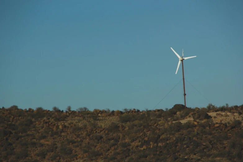 a wind turbine atop a hill is near the sky