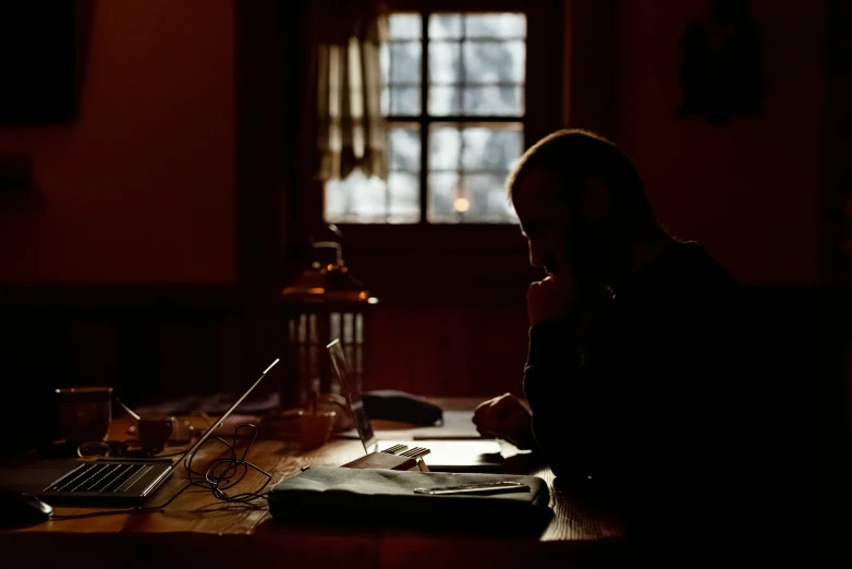a man with a book, laptop and glasses sits at a table