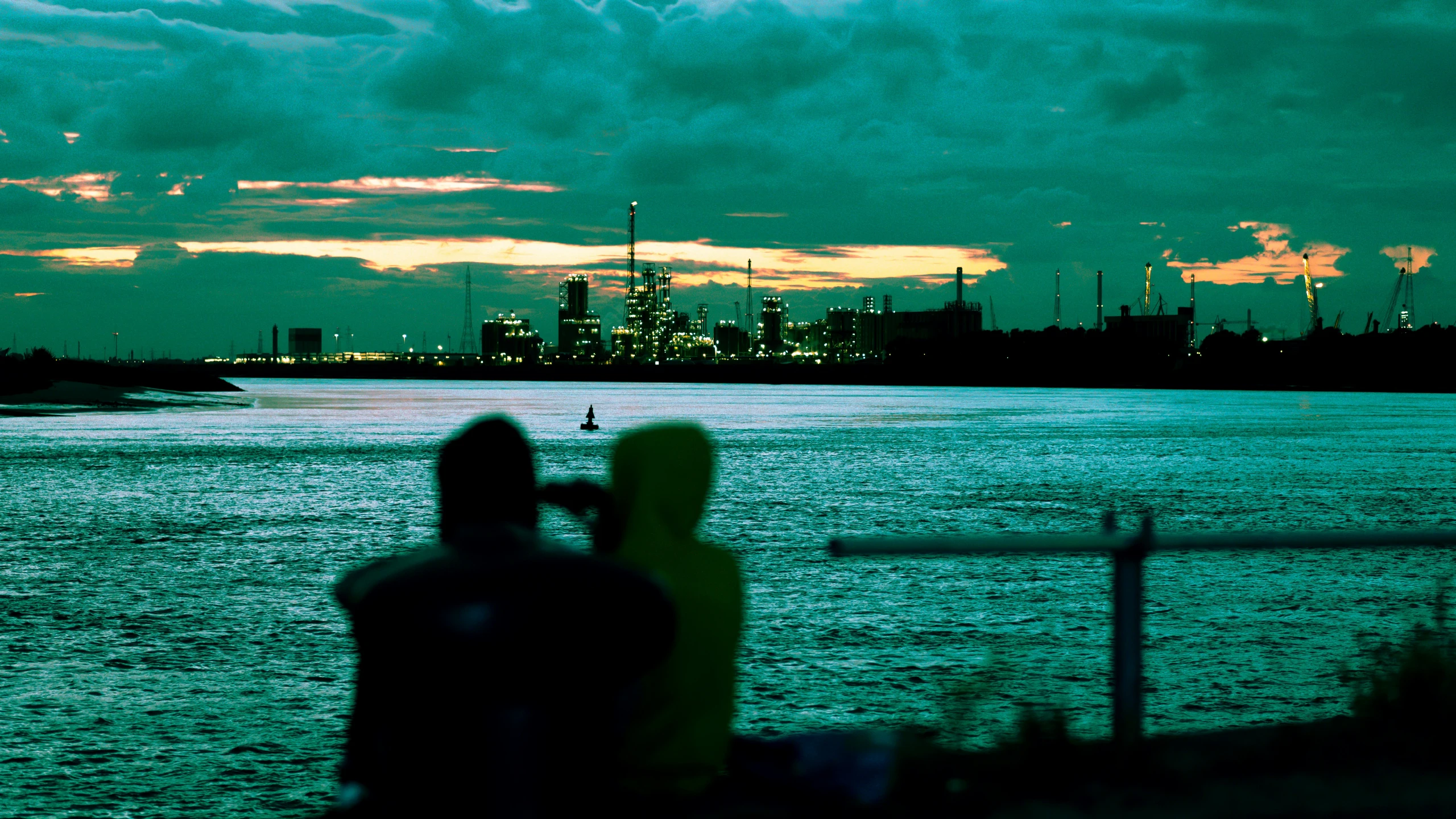 two people are sitting on the bench looking over a body of water