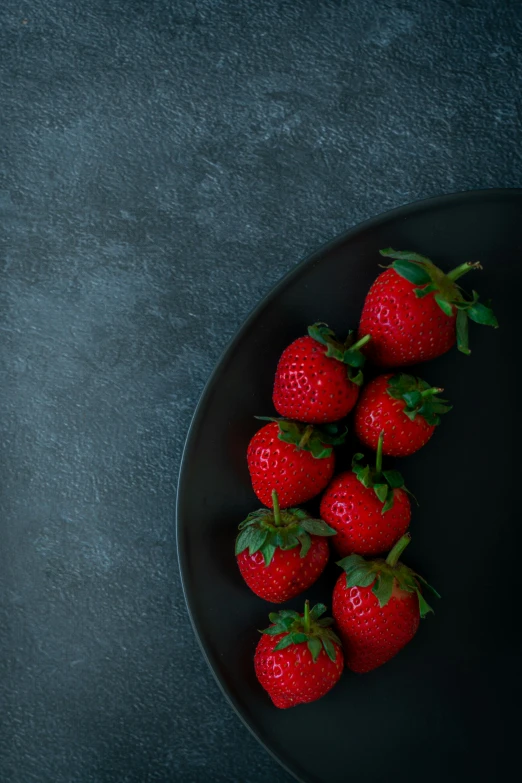 many strawberries sit in the black dish