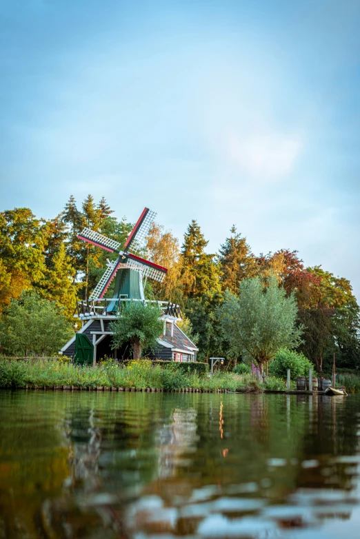 a mill sitting next to a lake surrounded by trees