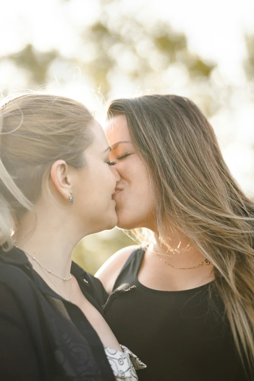 two women are kissing in front of trees