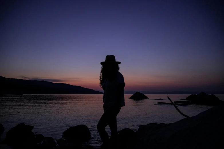 there is a woman standing near the water in the sunset