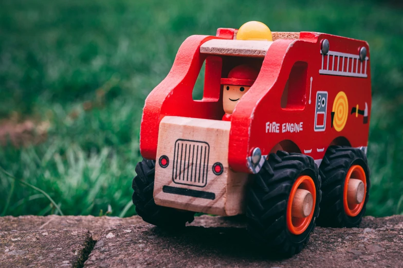 the toy fire truck is on the cement near some grass