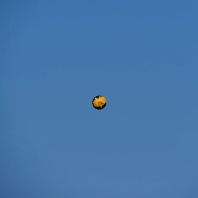 a large orange in the air in front of a blue sky