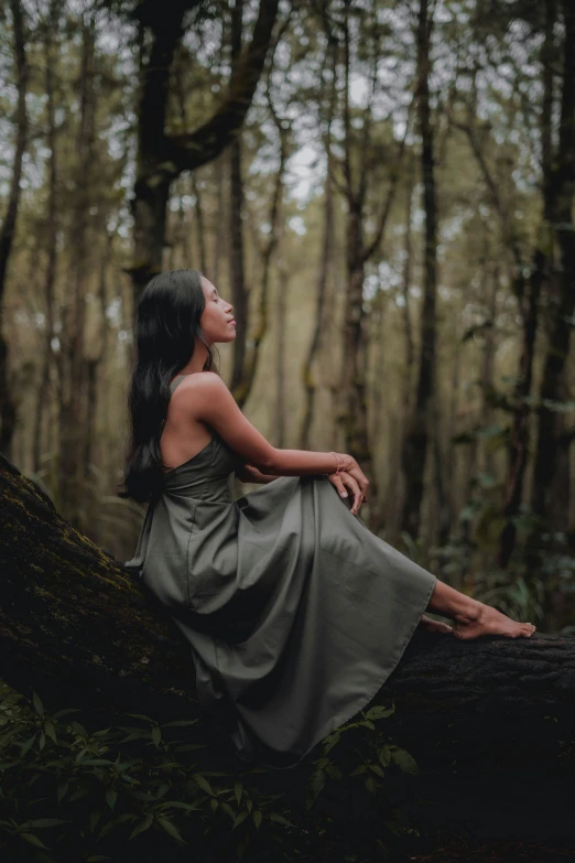 a woman sitting on a fallen tree in the woods