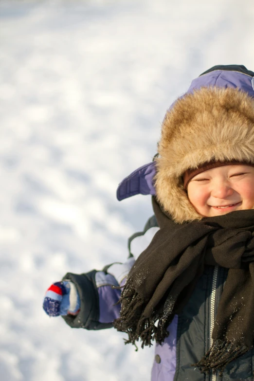 a boy in winter clothing and a hat playing in the snow