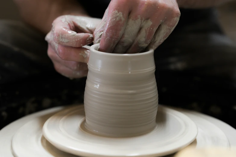 a person working on a pottery object with their hands