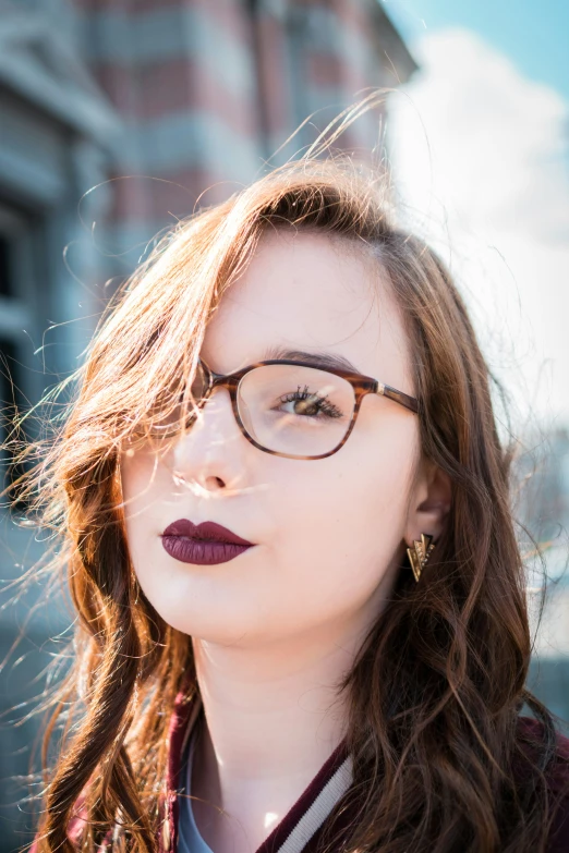 a woman with glasses posing in front of a brick building