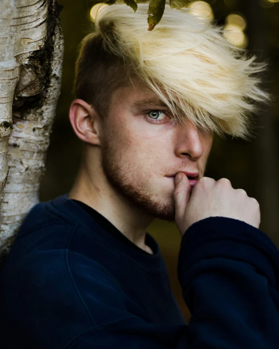 man with blonde hair and a long sleeved sweater posing