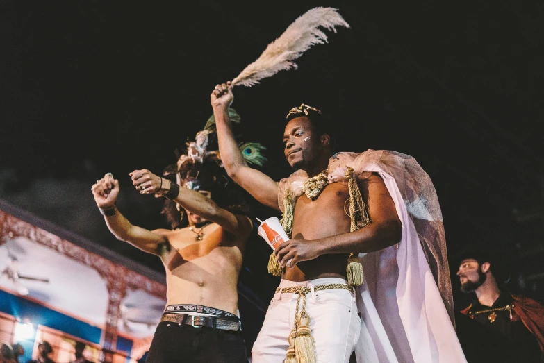 two men in white dance with feathers and make - up on their heads