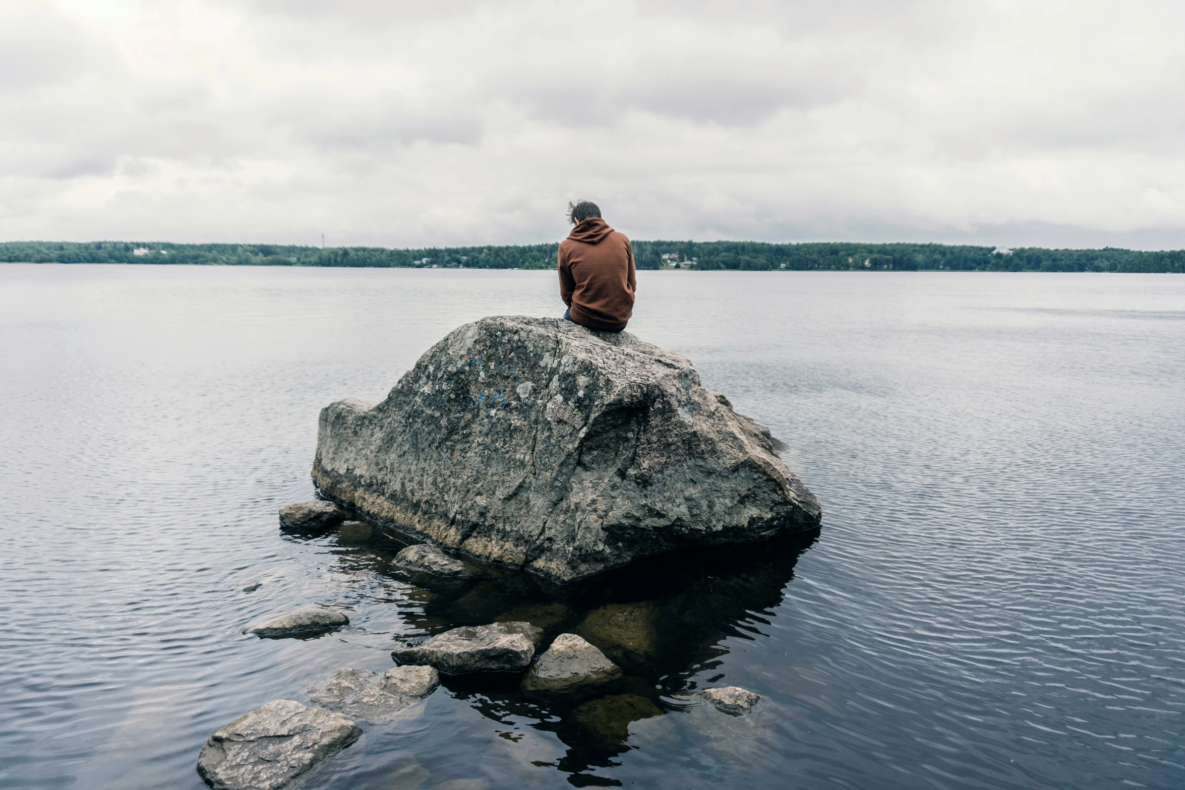 man in red jacket sitting on rock overlooking water and forest