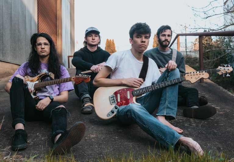 four musicians sit together in front of a building