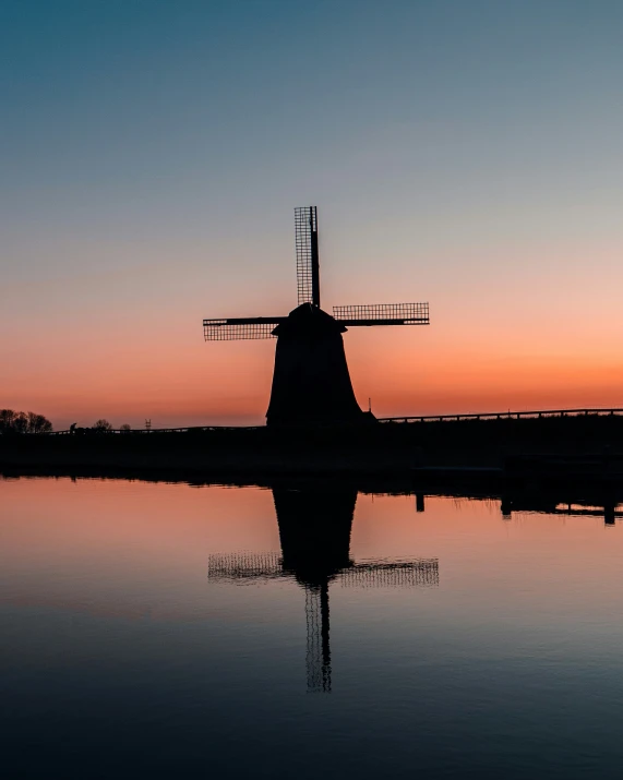 a windmill next to some water at sunset