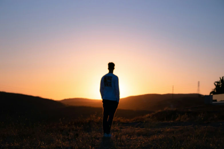 the person is standing on the field watching the sun rise