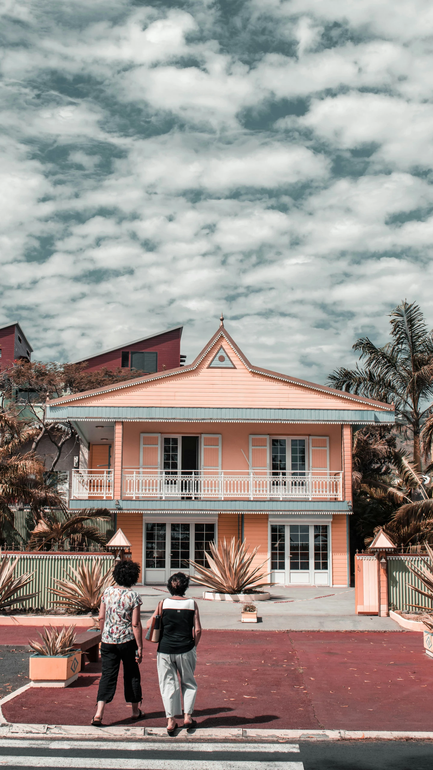 two women walking by a pink house with blue sky and clouds