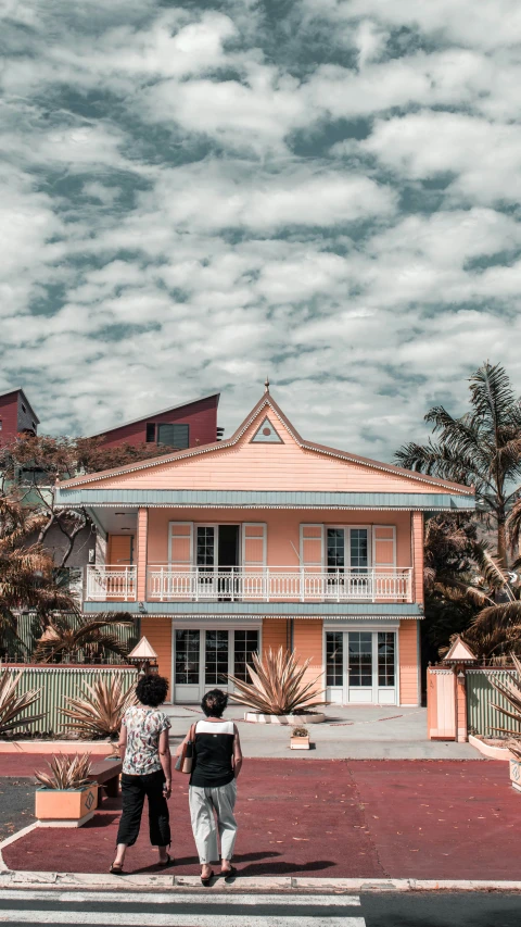 two women walking by a pink house with blue sky and clouds