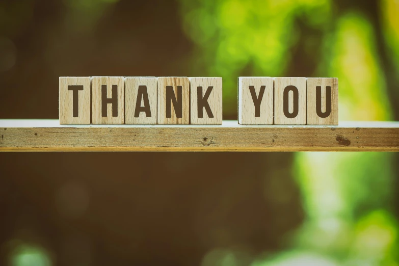 a block with the word thank you written on it sitting on top of a wooden table