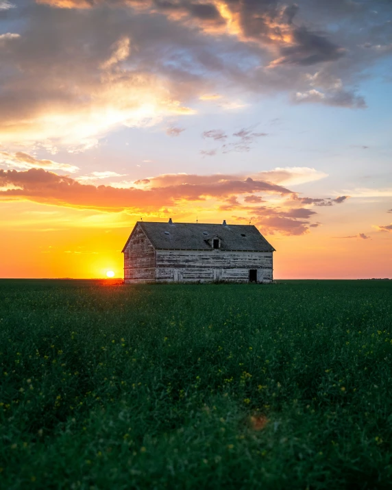 the sun sets over a white barn in a grassy field