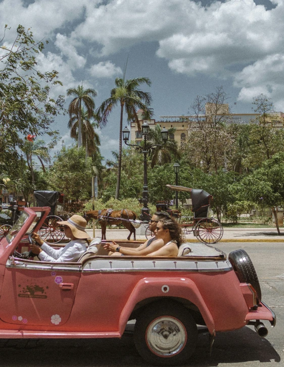 two people in the back of a convertible car, with trees and clouds