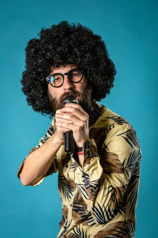 a man in sunglasses, curly hair and a afro, holds a microphone