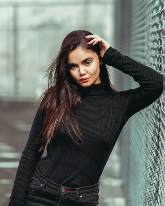 a woman leaning against a wall wearing a black top and jeans