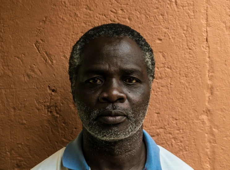 a man with black hair in front of a tan wall