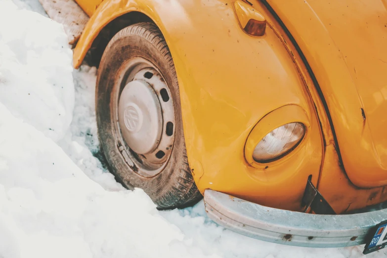 a close up of the nose of an old yellow beetle parked in snow