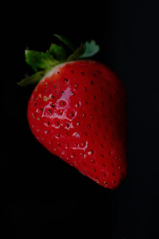 a red strawberry with a green stem on a black background