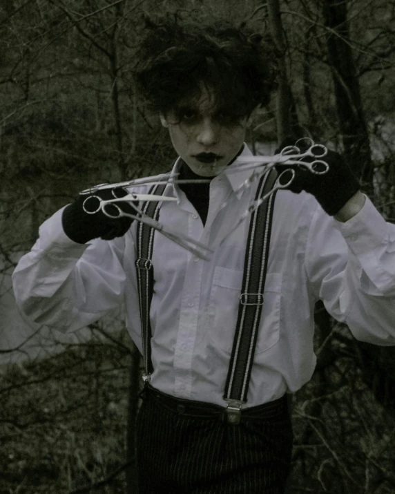 man in suspenders holding up scissors with both hands