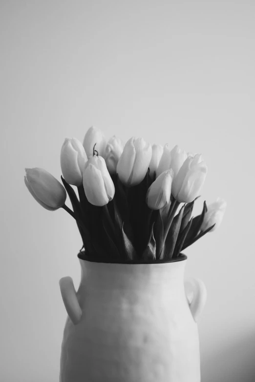 a white vase holds a bunch of white tulips