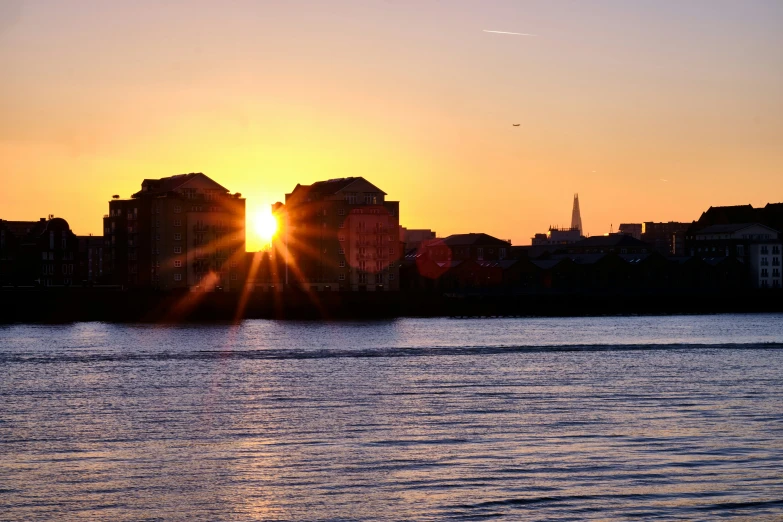 the setting sun lights up the horizon over the water in front of some large buildings