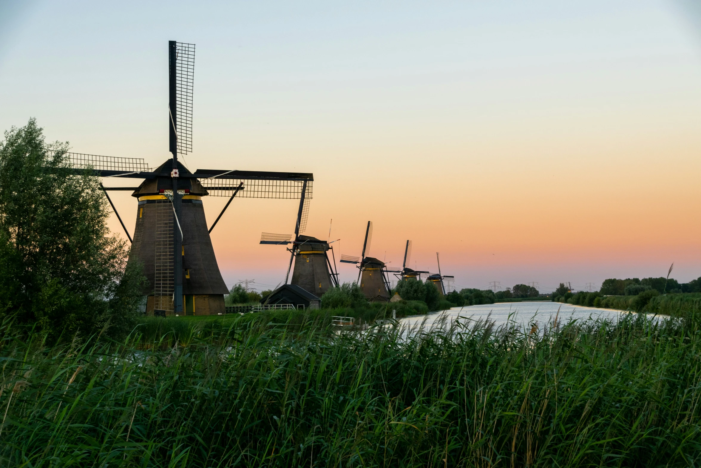 five windmills in the grass and a river