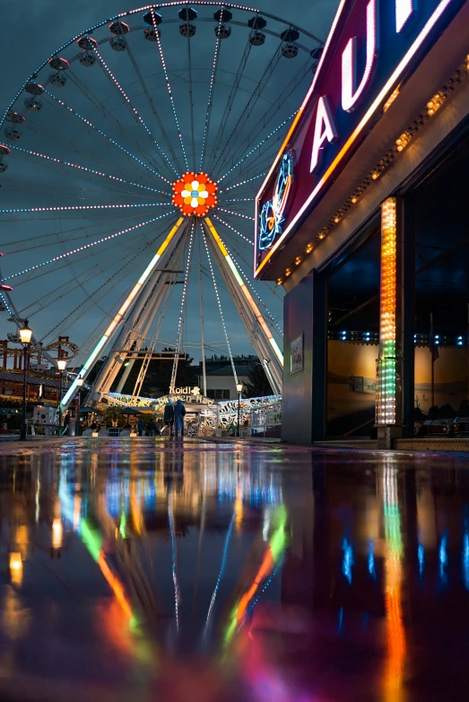 a ferris wheel at night with reflection on wet concrete