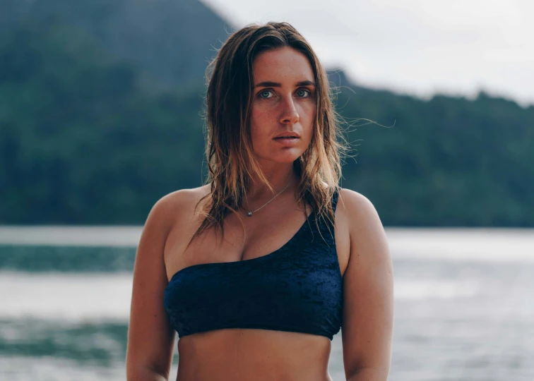 a woman standing in front of water wearing a bikini top