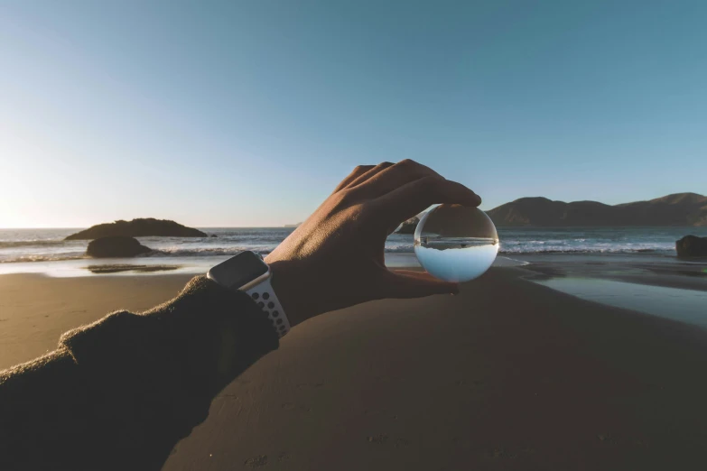 a hand holding up a wine glass on the beach