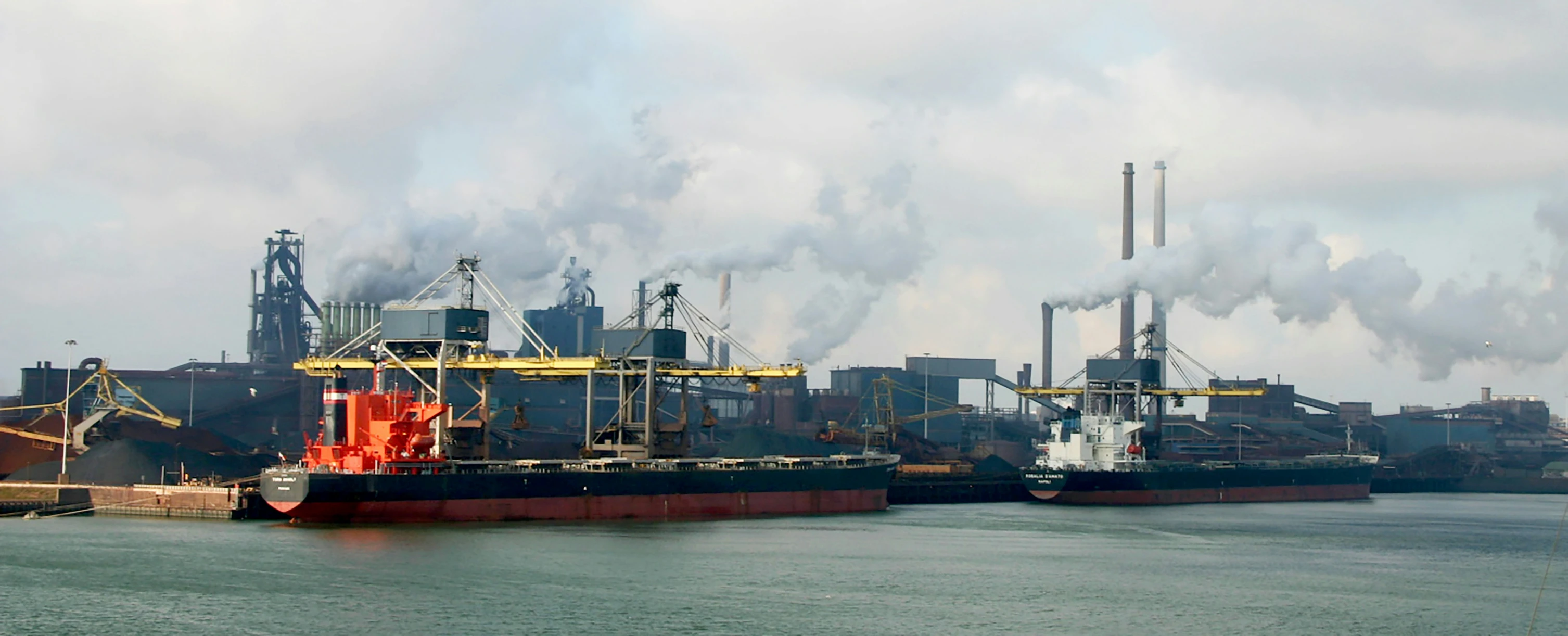 steam stacks up over a large port of industrial power plants