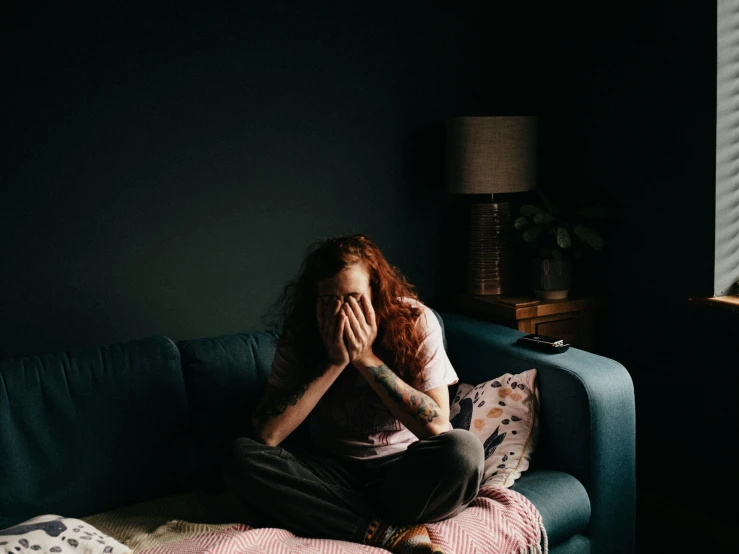 a woman sitting on a couch covering her face