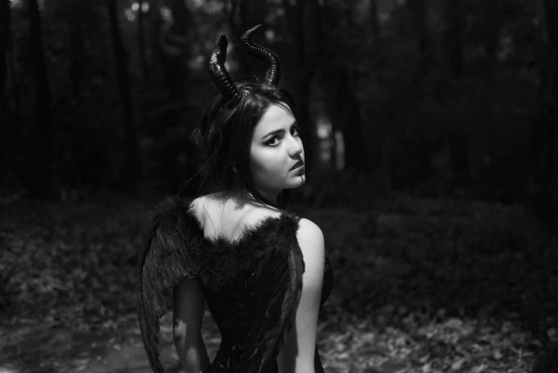 a girl with horns and wings stands in a forest