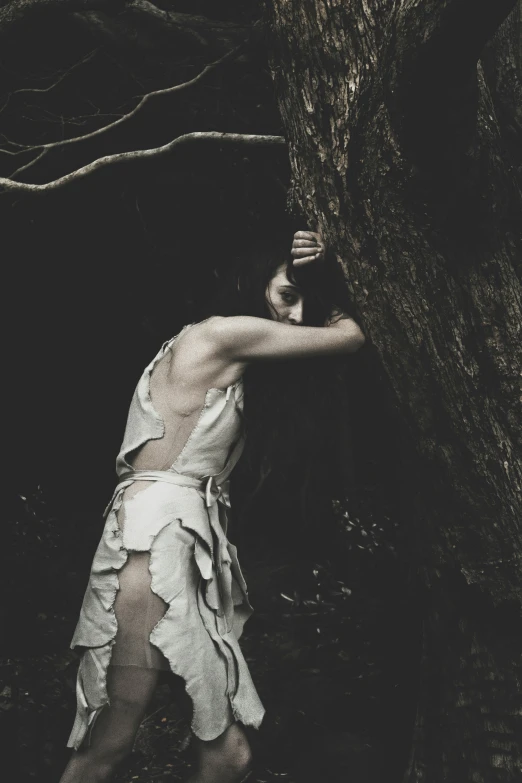 a woman holds on to the tree as she walks through a forest