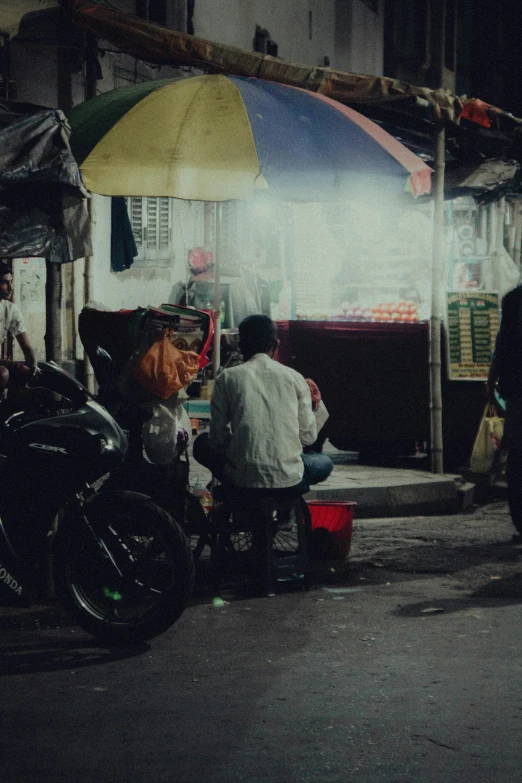 two men sitting in a city street with umbrellas on a building