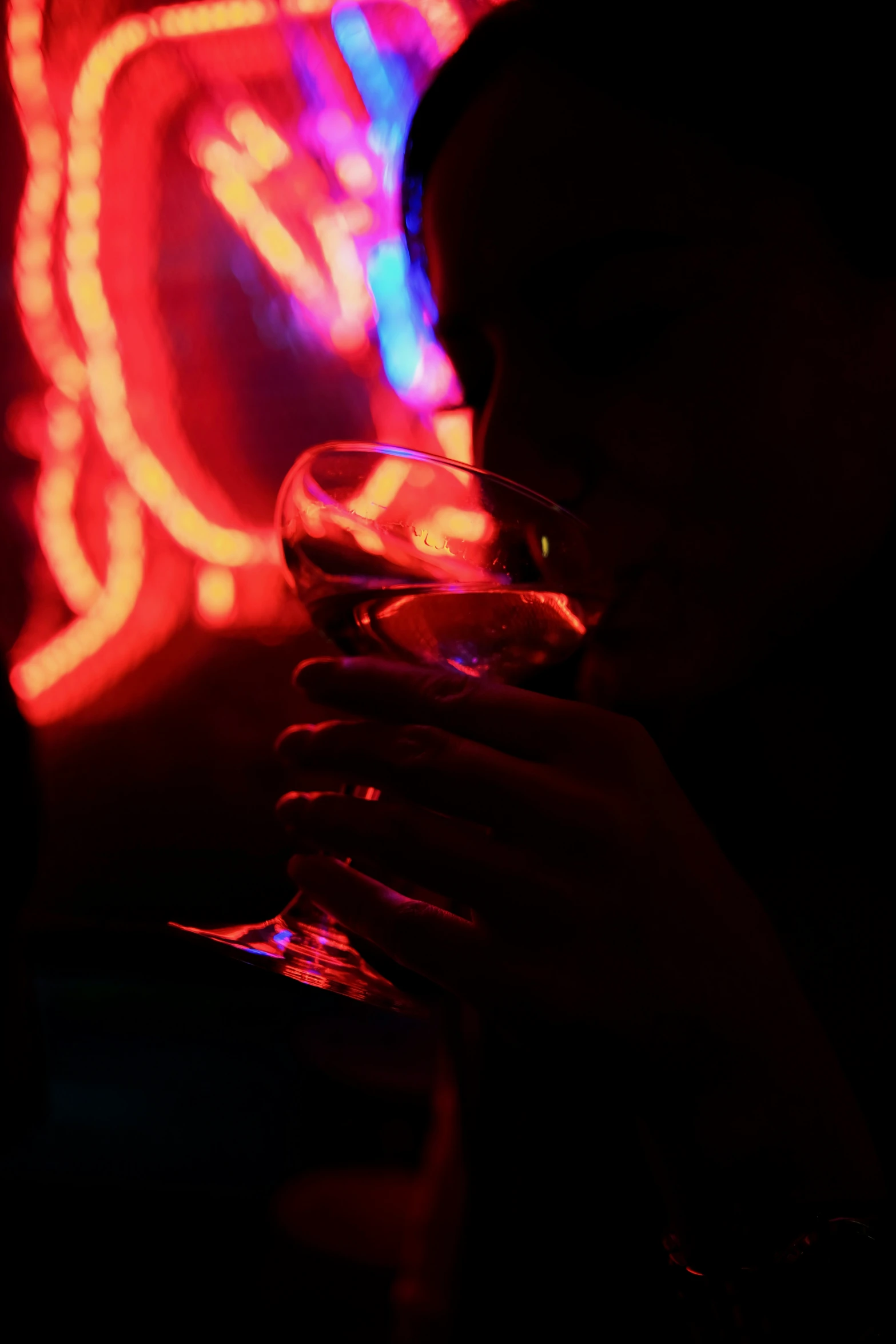 a woman drinking a glass of wine with red and blue lights behind her