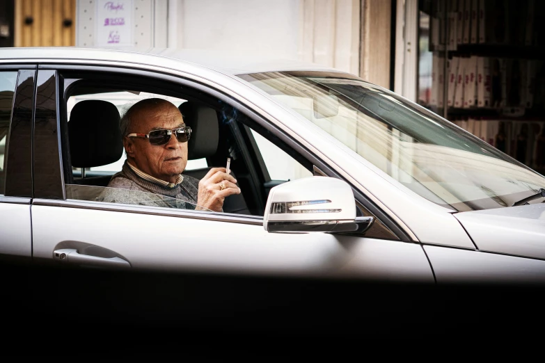 a man wearing sunglasses sits in his car and holds his cell phone