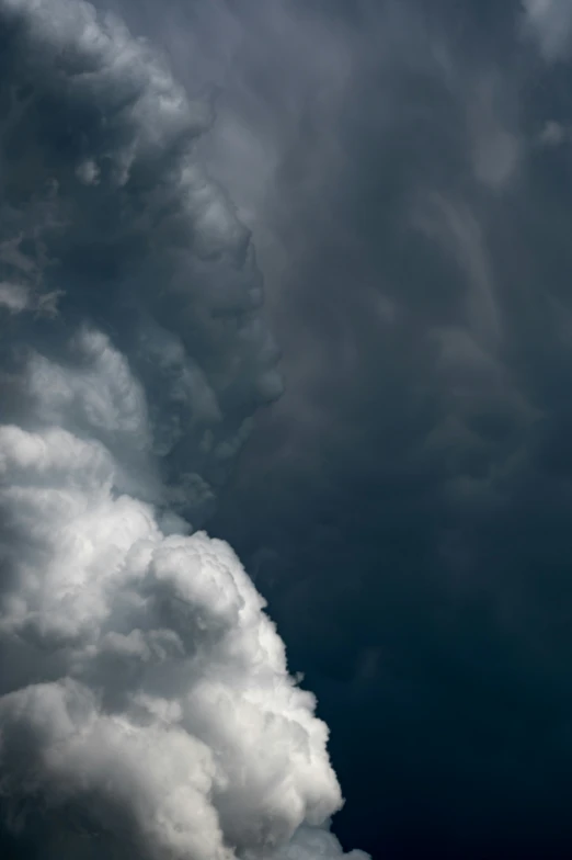 dark clouds roll through a cloudy sky with a single airplane flying in the foreground