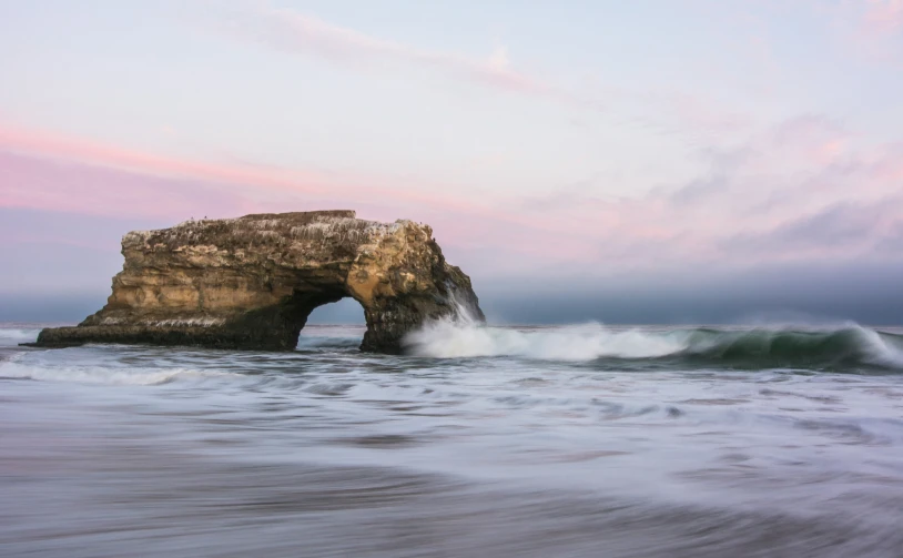 waves breaking over an ocean with a stone arch at dusk