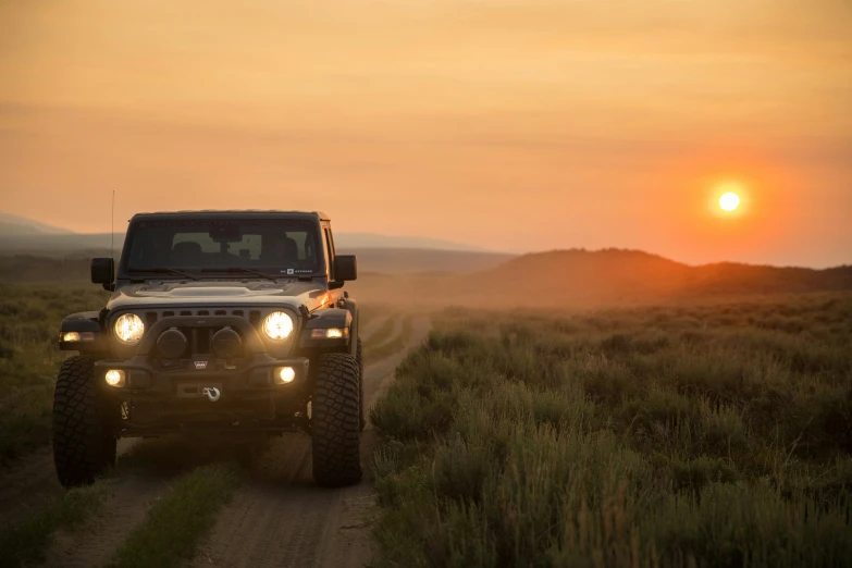 a jeep driving down a dirt road at sunset