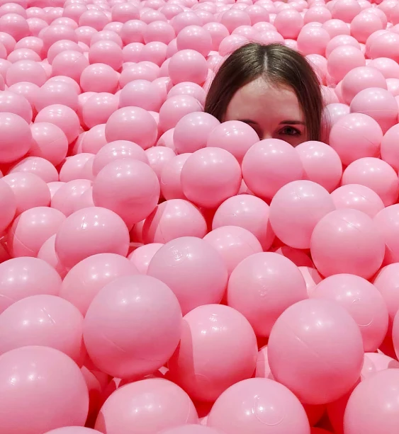 a girl is peeking out from a group of pink balls